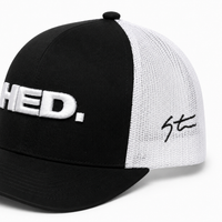 The HED. Trucker Snapback Hat – Black & White is an adjustable trucker hat featuring a black and white mesh design, “HED.” embroidered in large white letters on the front, and a bold black signature on the white mesh side.