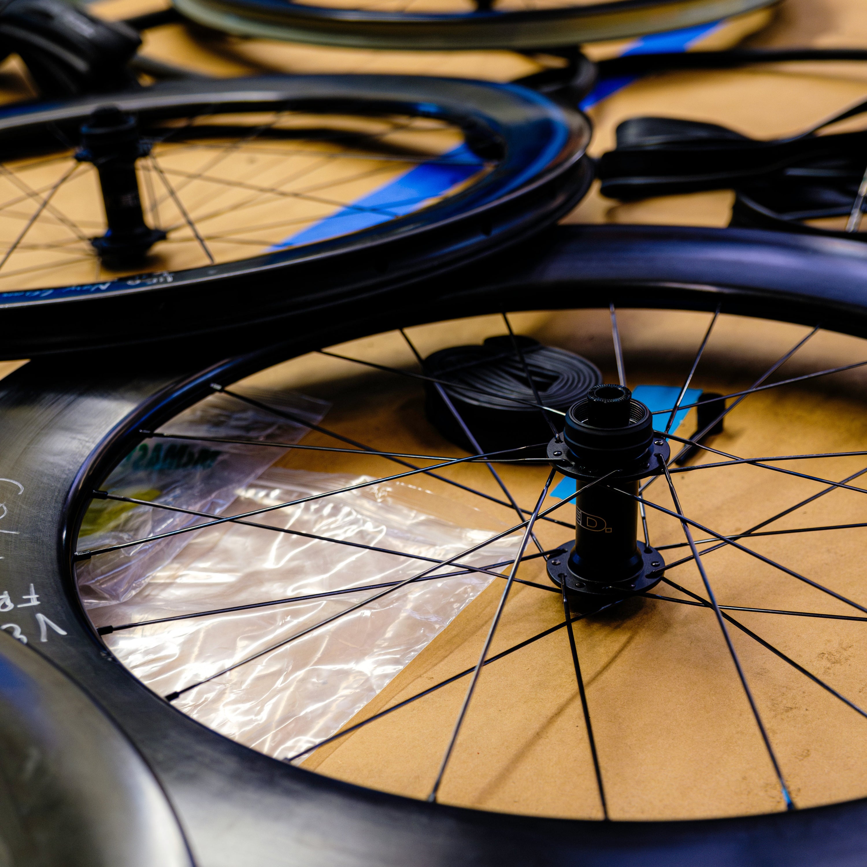 Several HED Vanquish V45 Carbon Aero 700c wheelsets in black carbon fiber with spokes are lying flat on a tan surface, overlapping each other. The new and clean wheels feature visible hubs, a 22.4 mm internal width, and some packaging material nearby.
